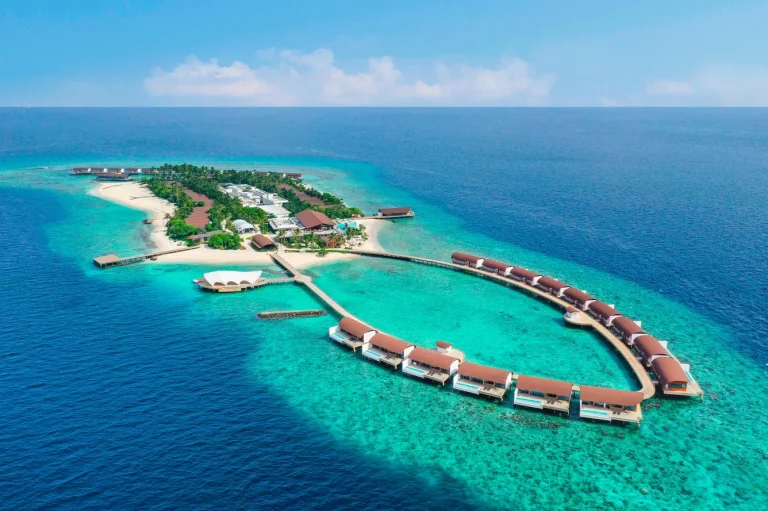 Aerial view of The Westin Maldives Miriandhoo island with a curved line of overwater villas and beach villas, Baa Atoll, Maldives