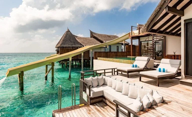 Overwater suite deck with day beds and a long yellow water slide into the lagoon at The OZEN Reserve Bolifushi, South Malé Atoll