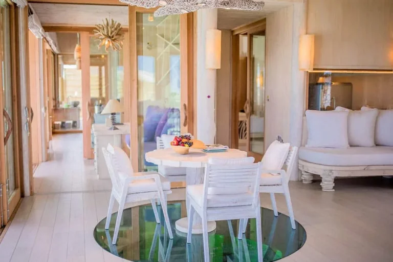 Living and dining room with a glass floor panel over the lagoon in a Soneva Jani 1-Bedroom Water Reserve with Slide, Noonu Atoll