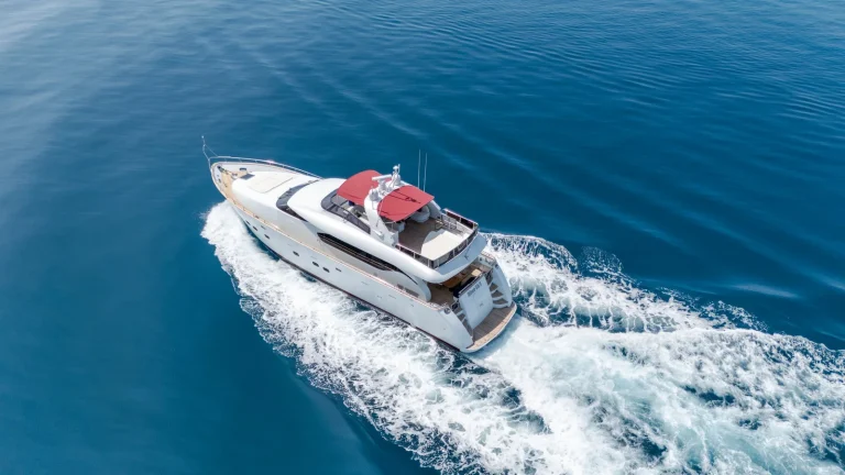 White motor yacht with a red sun canopy cruising across deep blue water, JOALI Maldives, Raa Atoll