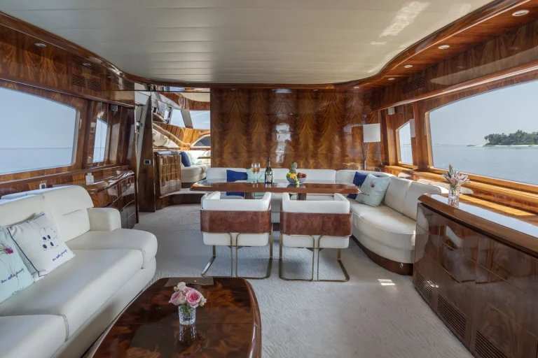 Yacht salon with cream sofas, polished timber panels and windows onto the sea, JOALI Maldives