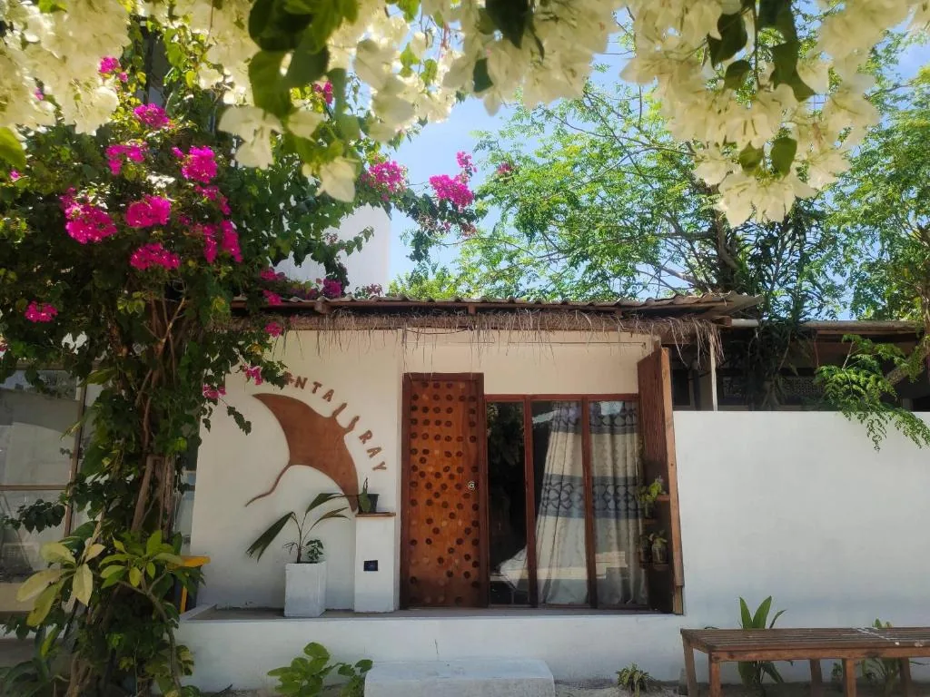 Tropical bungalow with bougainvillea, wooden round door with 'RAY' mural, sliding glass door and potted plants at Manta Ray, Fulidhoo, Maldives