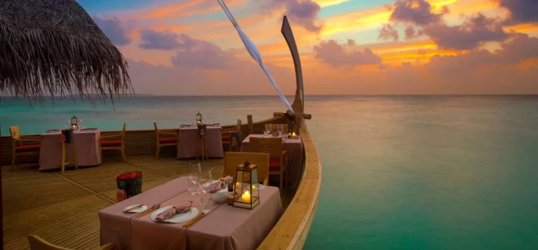 Tables set on an overwater deck with a sunset sky and sea, Milaidhoo Maldives, Maldives
