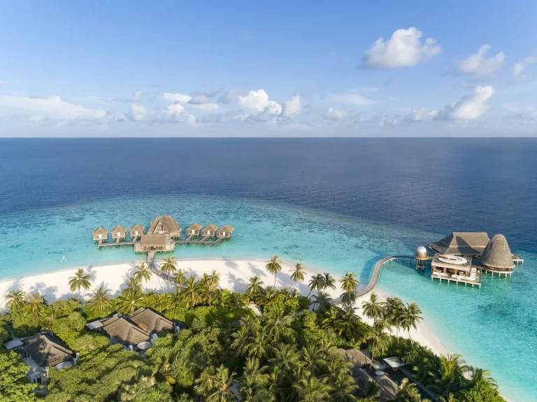 Aerial view of Anantara Kihavah Maldives Villas island in Baa Atoll with beach villas under palms and overwater pool villas reaching out over the lagoon