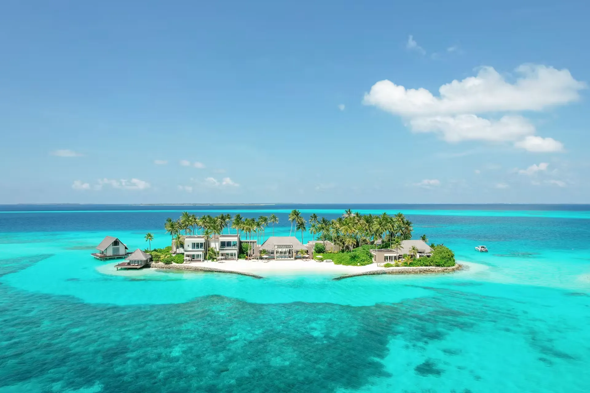 Aerial view of the Cheval Blanc Randheli Private Island, a small palm-covered islet with villas and a white sand rim in a turquoise lagoon, Noonu Atoll, Maldives