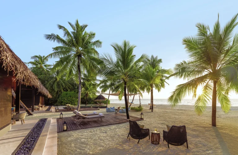 Outdoor living area of a One&Only Reethi Rah two-villa residence with loungers, dining chairs and palms on a private white sand beach, North MalΓ© Atoll