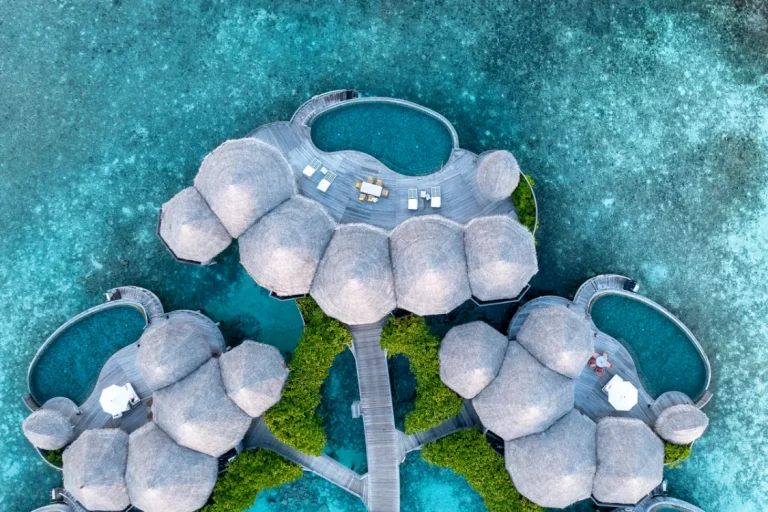 Top-down aerial of The Nautilus Maldives ocean houses with round thatched roofs and circular private pools over a turquoise lagoon, Baa Atoll