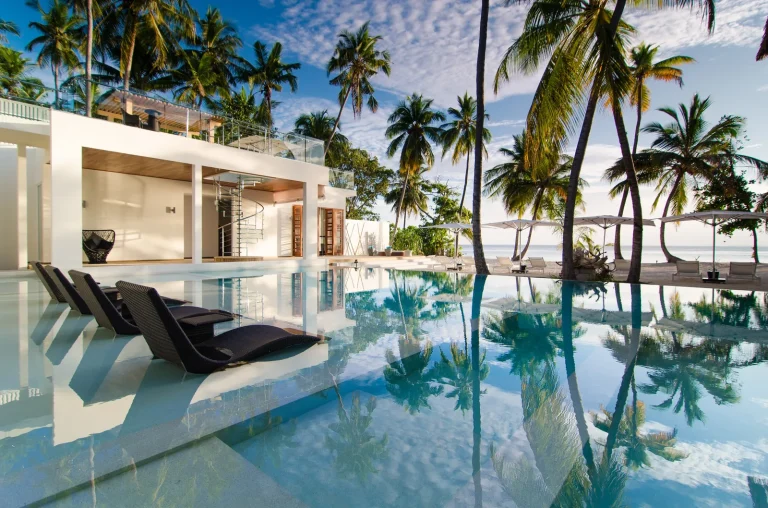 Long private infinity pool reflecting palms in front of a modern white residence at Amilla Maldives, Baa Atoll