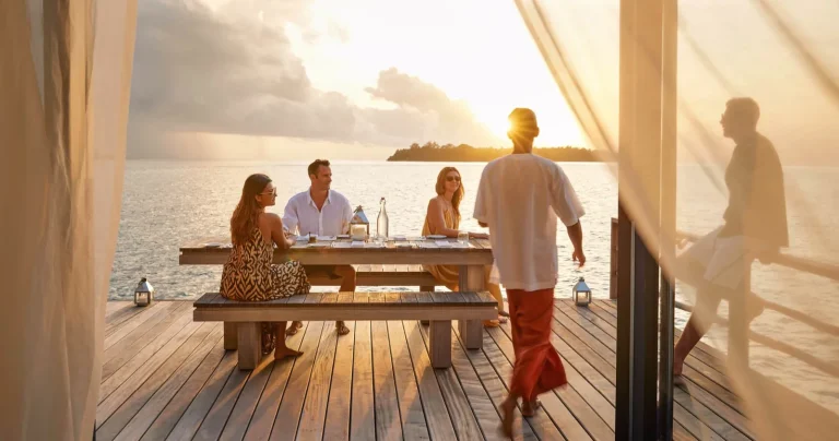Family dining at sunset on the overwater deck of the Three-bedroom COMO Sunset Villa at COMO Cocoa Island, South MalΓ© Atoll, Maldives