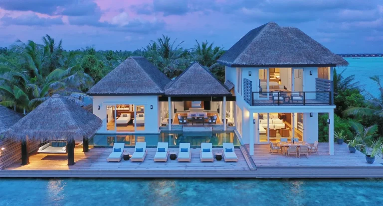 Two-storey Naladhu Two Bedroom Beach Pool Residence lit at twilight with a long pool and loungers, South MalΓ© Atoll, Maldives