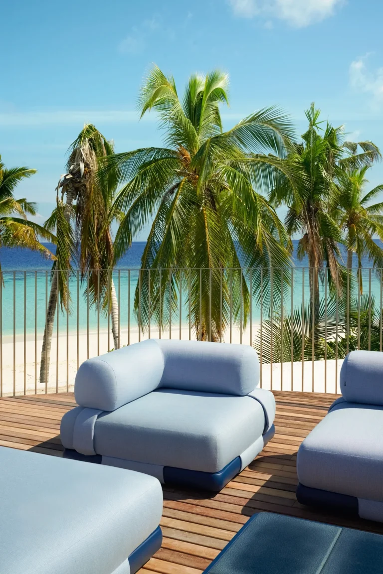 Blue outdoor sofas on a timber deck under palms beside the beach, Nilaa Coral Island, Maldives
