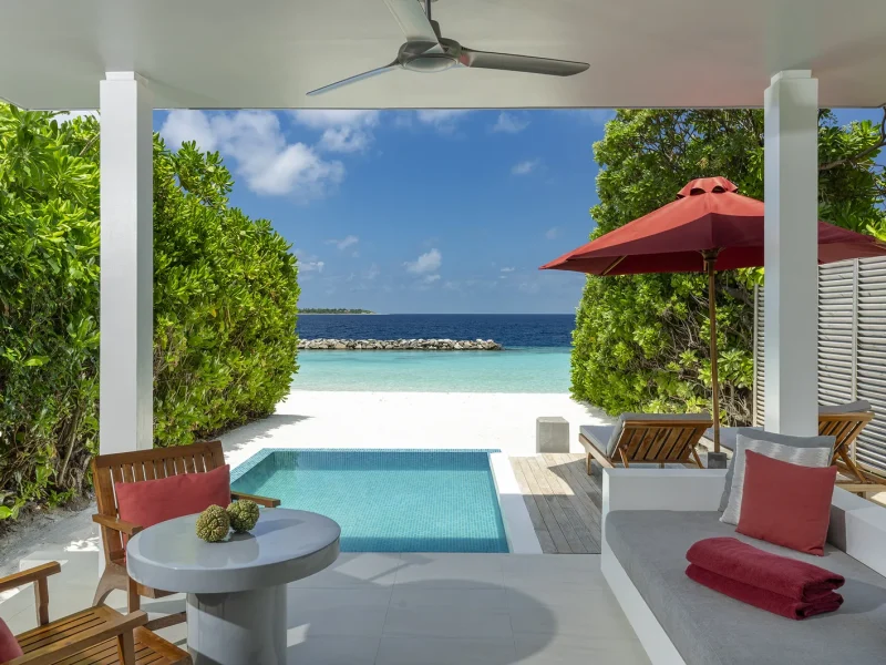 Covered terrace with red cushions and a plunge pool looking out to the beach and lagoon at a Beach Villa with Pool, Niva Dhigali Maldives