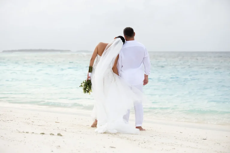 Bride and groom walking along a white beach by the turquoise lagoon at Niva Dhigali Maldives