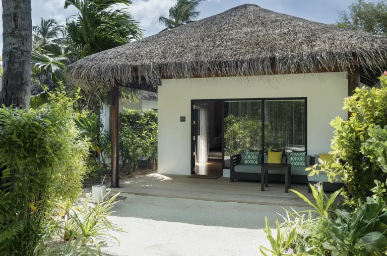 Thatched villa with sliding doors and a shaded terrace on white sand among tropical plants, Niva Velassaru Maldives