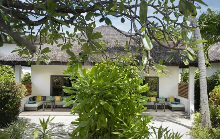 Thatched villa with a terrace and sofas set in a tropical garden at a Two Bedroom Deluxe Villa, Niva Velassaru Maldives