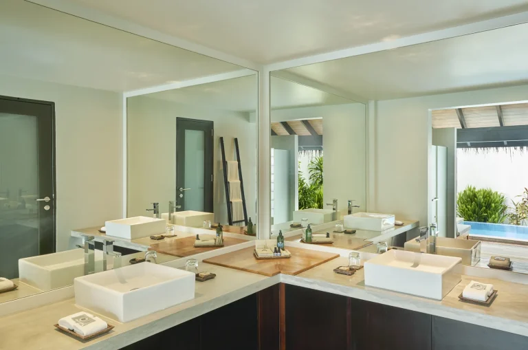 Marble bathroom with twin rectangular basins, large mirrors and a view through to a private pool, Niva Velassaru Maldives