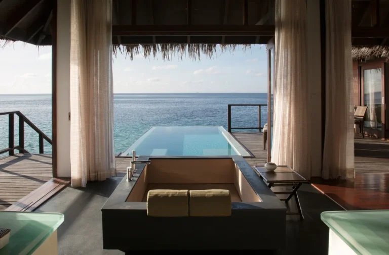 View from the bedroom of a Coco Bodu Hithi Water Villa through to a glass-edged private pool and the open lagoon, North MalΓ© Atoll, Maldives