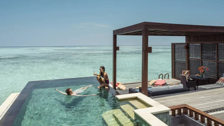 Couple swimming in the infinity pool of an overwater Water Villa with Pool at Four Seasons Resort Maldives at Kuda Huraa, North MalΓ© Atoll