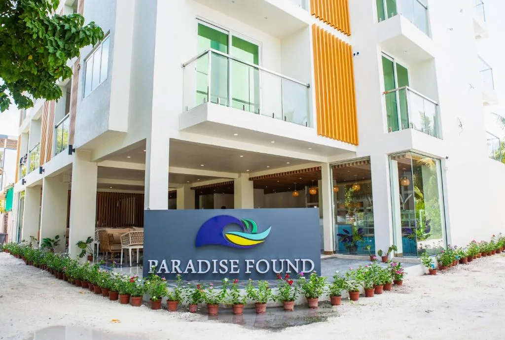 White two-story Paradise Found with orange-striped canopy, glass-front lobby, balcony rooms and potted plants at Paradise Found, Dhigurah, Maldives