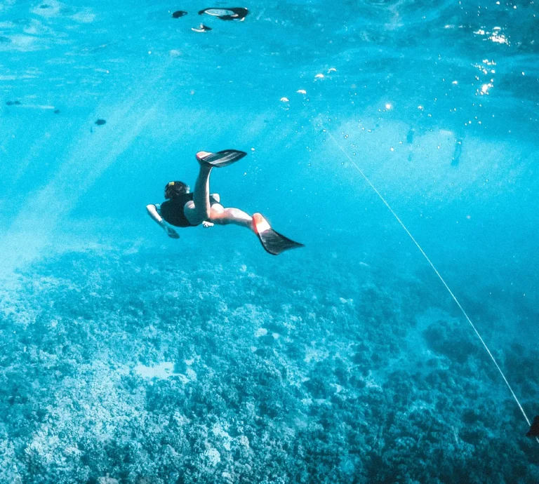 Freediver swimming down through clear blue water toward the reef in the Fari Islands, Maldives