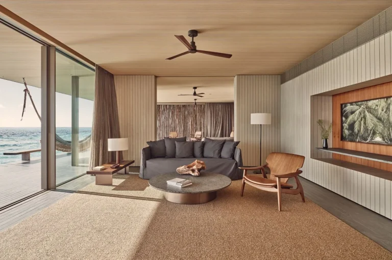 Living room with a low sofa, timber ceiling and glass doors open to the ocean in a sunset villa at Patina Maldives