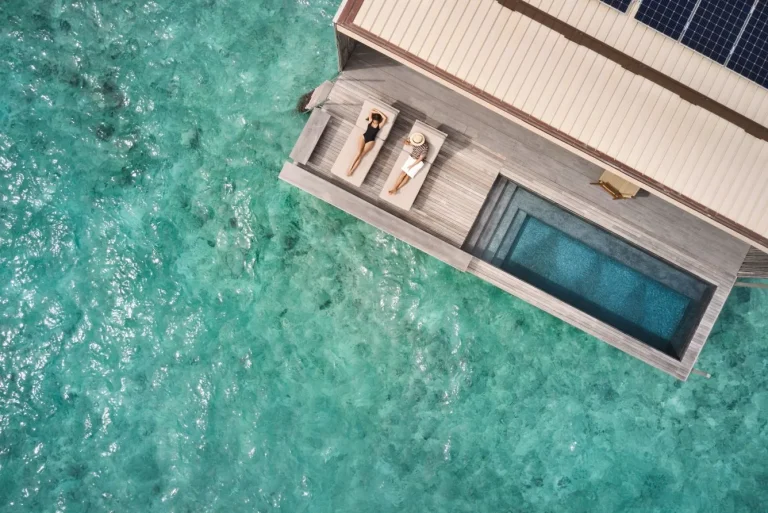 Overhead view of an overwater villa deck with a private pool and sunbeds above clear turquoise water at Patina Maldives