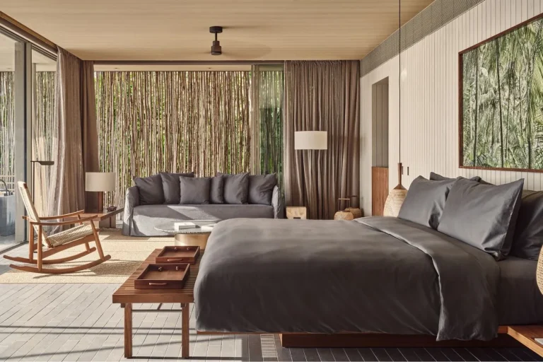 Bedroom with a grey linen bed, timber floors and floor-to-ceiling glass in a water pool villa at Patina Maldives