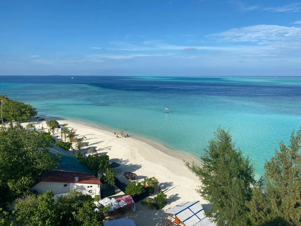 White-sand beach with turquoise lagoon, shallow reef and overwater bungalows seen from a hillside at Pearlshine Retreat Maldives, Gulhi, Maldives