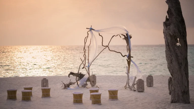 Driftwood arch and low seating arranged on the beach at sunset for a private event at Four Seasons Private Island Maldives at Voavah, Baa Atoll
