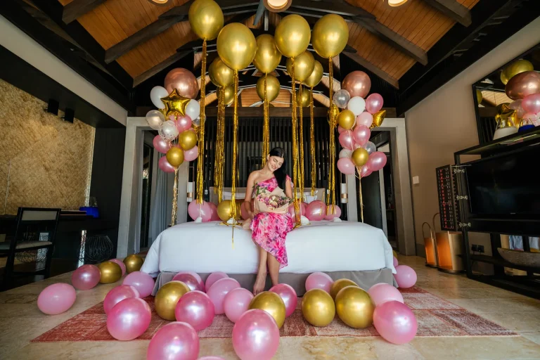 Child in a pink dress standing among pink and gold balloons and a gold balloon arch in a villa bedroom decorated for a birthday at Velaa Private Island