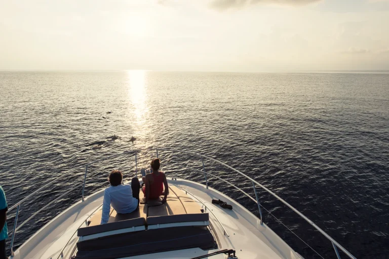 Two guests sitting on the bow of a yacht watching the sunset over a calm Indian Ocean on a dolphin cruise from Velaa Private Island, Noonu Atoll