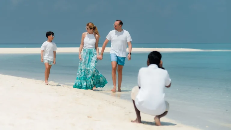Family walking on the white sand beach of Four Seasons Private Island at Voavah while a team member takes their photo, Baa Atoll UNESCO Biosphere Reserve