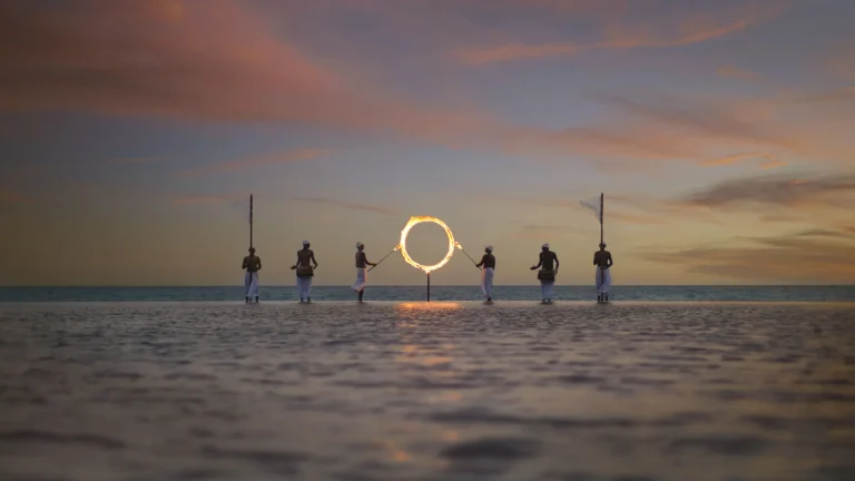 Silhouettes of performers around a glowing ring of fire in the lagoon at sunset at EAU Bar, The Ritz-Carlton Maldives, Fari Islands