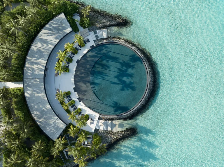Aerial view of a curved bar building around a circular infinity pool among palms at EAU Bar, The Ritz-Carlton Maldives, Fari Islands