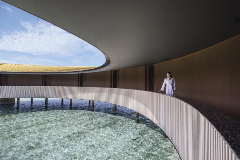 Curved walkway with a circular opening framing the sky above a lagoon at The Ritz-Carlton Spa, Fari Islands