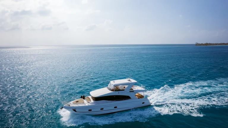 Aerial view of a white motor yacht leaving a wake across blue water off a low island, The Ritz-Carlton Maldives, Fari Islands