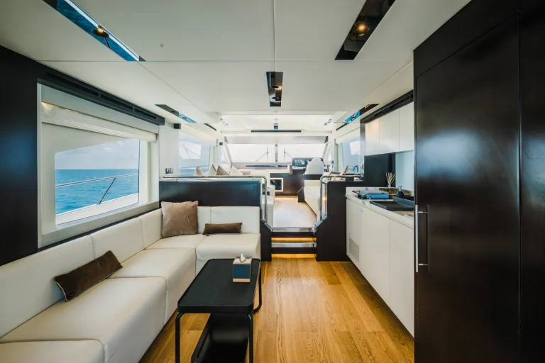 Bright yacht salon with white sofas, timber floor, galley and wide windows, The Ritz-Carlton Maldives, Fari Islands