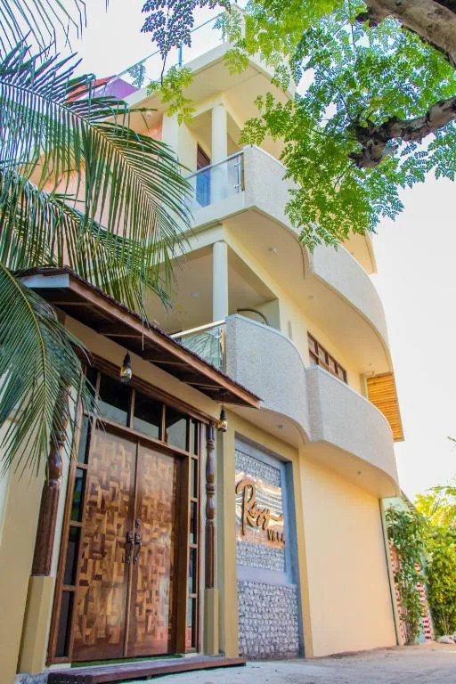 Three-story Villa with carved wooden double doors, glass-railed balcony, stone-clad wall and palm-lined entrance at Rosy Villa Hotel, Guraidhoo, Maldives