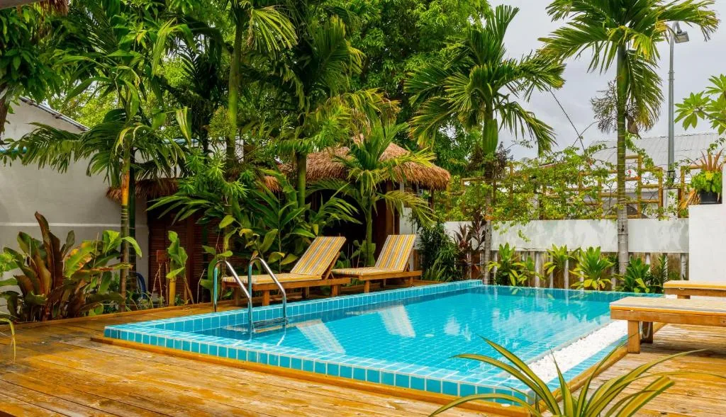 Outdoor pool with turquoise tiled deck, stainless ladder, two yellow sun loungers and thatched palapa amid tropical palms at Shark Lounge, Fuvahmulah, Maldives