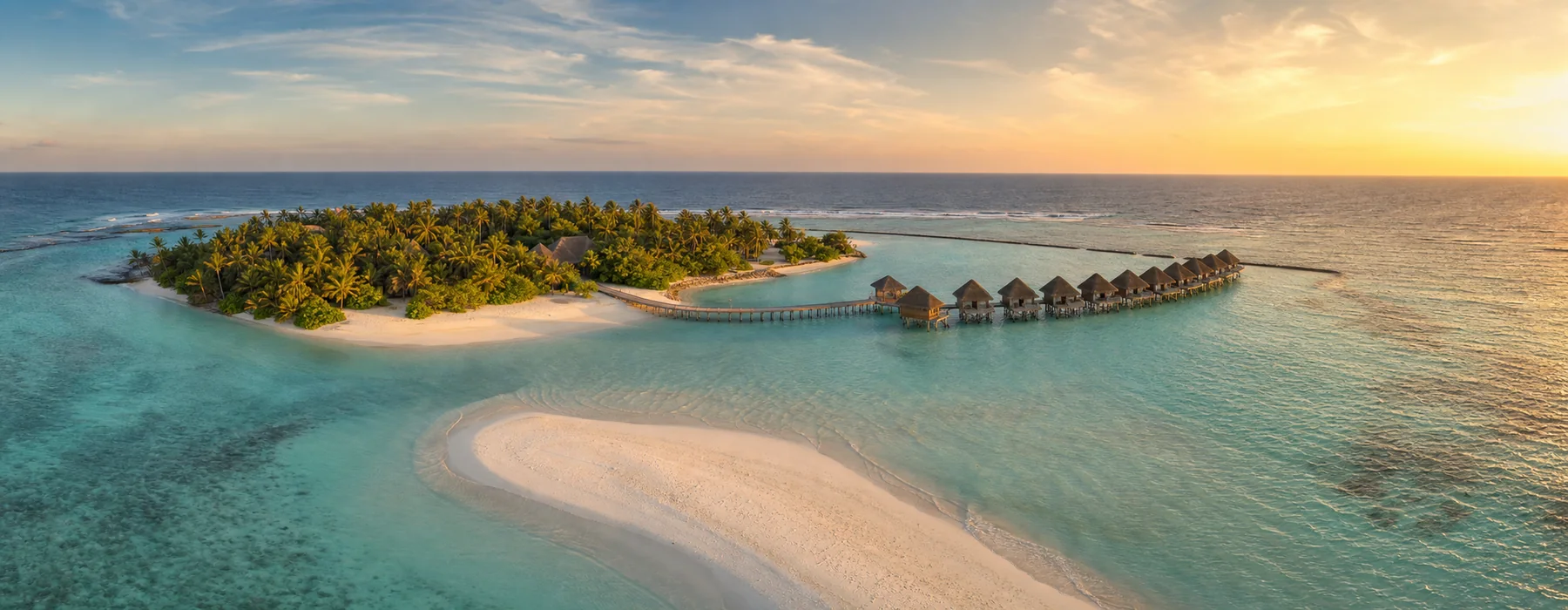 Aerial view of a Maldives resort island with overwater villas, white sandbank and turquoise lagoon at golden hour