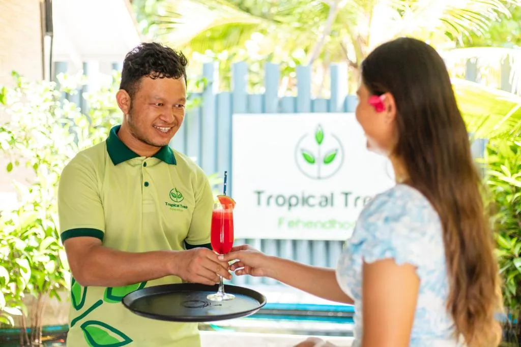Man holding a tray with a woman holding a drink at Tropical Tree, Fehendhoo, Maldives