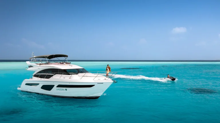 White motor yacht anchored in a turquoise lagoon with a guest on a jet ski beside it, Velaa Private Island, Noonu Atoll