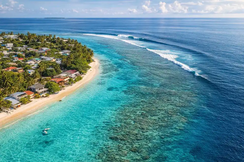 Aerial view of a Maldivian local island with guesthouses on the beach and a peeling reef wave offshore